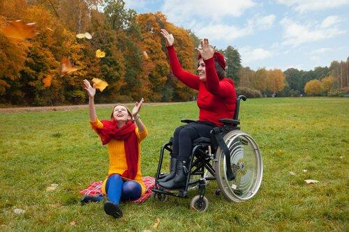 tekerlekli sandalyede bir kadın ve arkadaşı çimlerde