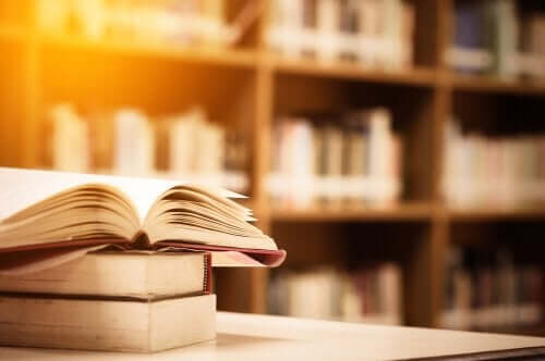 Biri açık olan üç kitap ve arka planda kitap rafları.