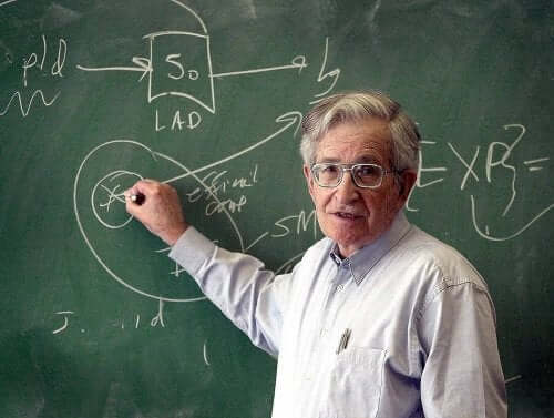 Noam Chomsky bir tahtaya bir şeyler yazarken poz veriyor.