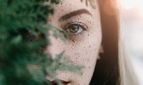 Ağaç dallarının arkasından bakan bir kadın.