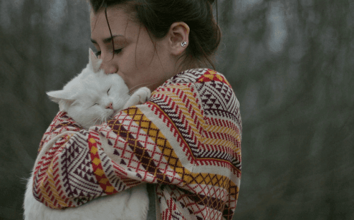 Bir kediyi kucaklamış, öpen bir kadın.