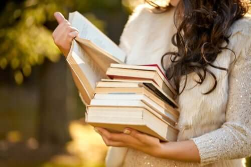 Elinde bir sürü kitap tutan, kitaplardan birini okuyan bir kadın.