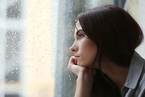 Dışarıda yağmur yağarken camın önünde oturan bir kadın.