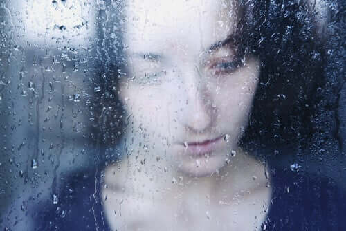 Üstünde yağmur damlaları olan camdan dışarı bakan kadın