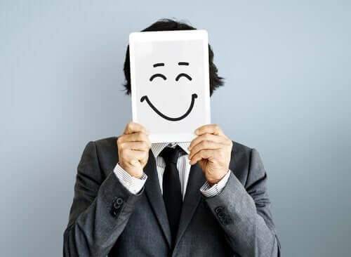 Üzerinde mutlu bir surat olan bir kağıdı yüzünün önünde tutan bir adam.