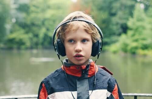 Doğanın içerisindeki bir alanda kulaklıkla müzik dinleyen otizmli çocuk.