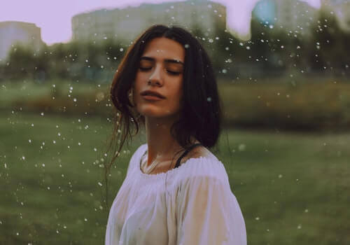 Gözleri kapalı bir şekilde, dışarıda yağmurun altında duran bir kadın.