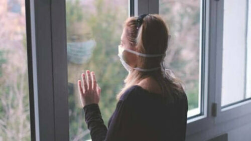 Yüzünde maske ile pencereden bakan bir kadın.