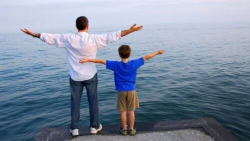 Kollarını açarak denize bakan bir çocuk ve bir yetişkin.
