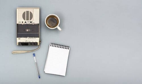 Bir kayıt cihazı, bir kupa kahve, bir kalem ve bir defter.