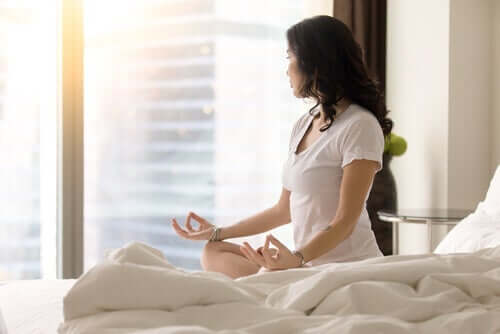Yatağında oturmuş meditasyon yapan bir kadın.