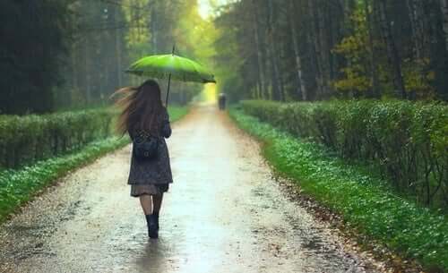 yağmurlu günde yeşil şemsiyeyle ormanlık alanda yürüyen kadın