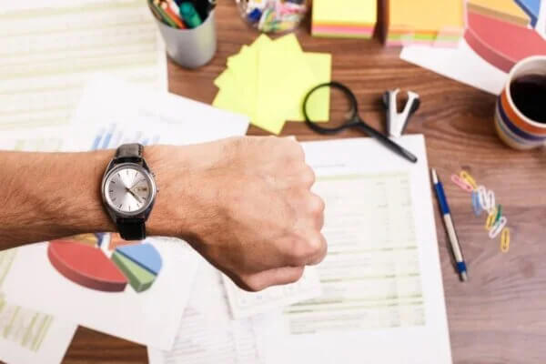 çalışma masasında saatine bakan adam