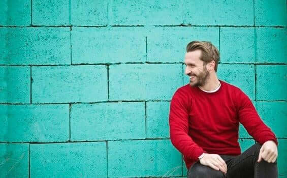 mavi duvarın önünde oturmuş gülümseyen kırmızı kazaklı adam