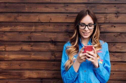 duvara dayanmış telefonuna gülümseyen kız