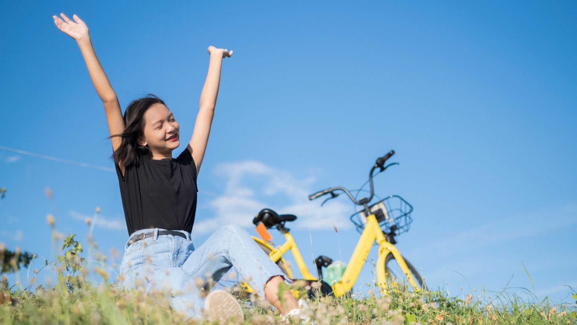 çimlerde oturan sarı bisikletli mutlu kadın